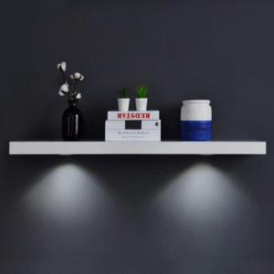 A sleek white floating shelf with decorative items and built-in spotlights illuminating below.
